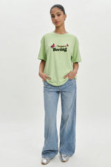 Person wearing a light green t-shirt with text and blue jeans on a white background.pastel green oversized t-shirt, normal is boring graphic tee, butterfly back print t-shirt, floral aesthetic oversized tee, dopamine dressing outfit, gen z streetwear india, oversized cotton graphic t-shirt women, aesthetic back print tee, casual summer oversized t-shirt, trendy statement t-shirt