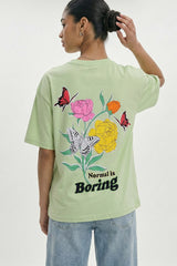 Person wearing a light green t-shirt with floral and butterfly design and 'Normal is Boring' text.pastel green oversized t-shirt, normal is boring graphic tee, butterfly back print t-shirt, floral aesthetic oversized tee, dopamine dressing outfit, gen z streetwear india, oversized cotton graphic t-shirt women, aesthetic back print tee, casual summer oversized t-shirt, trendy statement t-shirt.