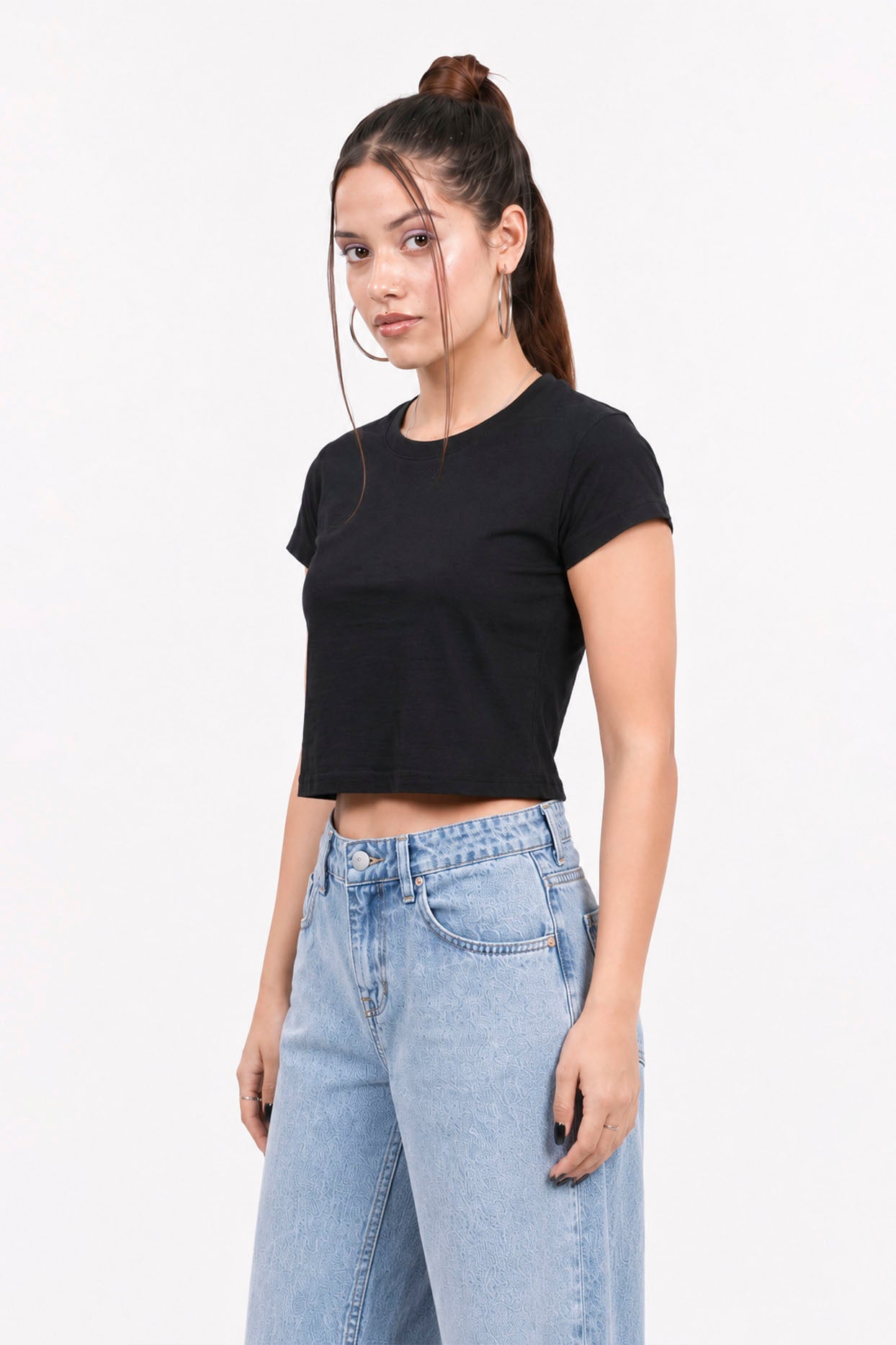 Woman wearing a black crop top and light blue jeans on a white background.black crop top, black crop top women, women's black crop top, black top for women, trendy black crop top, stylish black crop top, casual black crop top, fitted crop top, cropped top women, sleeveless black top, black fashion top, women's fashion top, ladies black top, black crop tank top, summer crop top, trendy women's clothing, casual women's wear, street style outfit, black crop top outfit, blue jeans outfit, gym top.