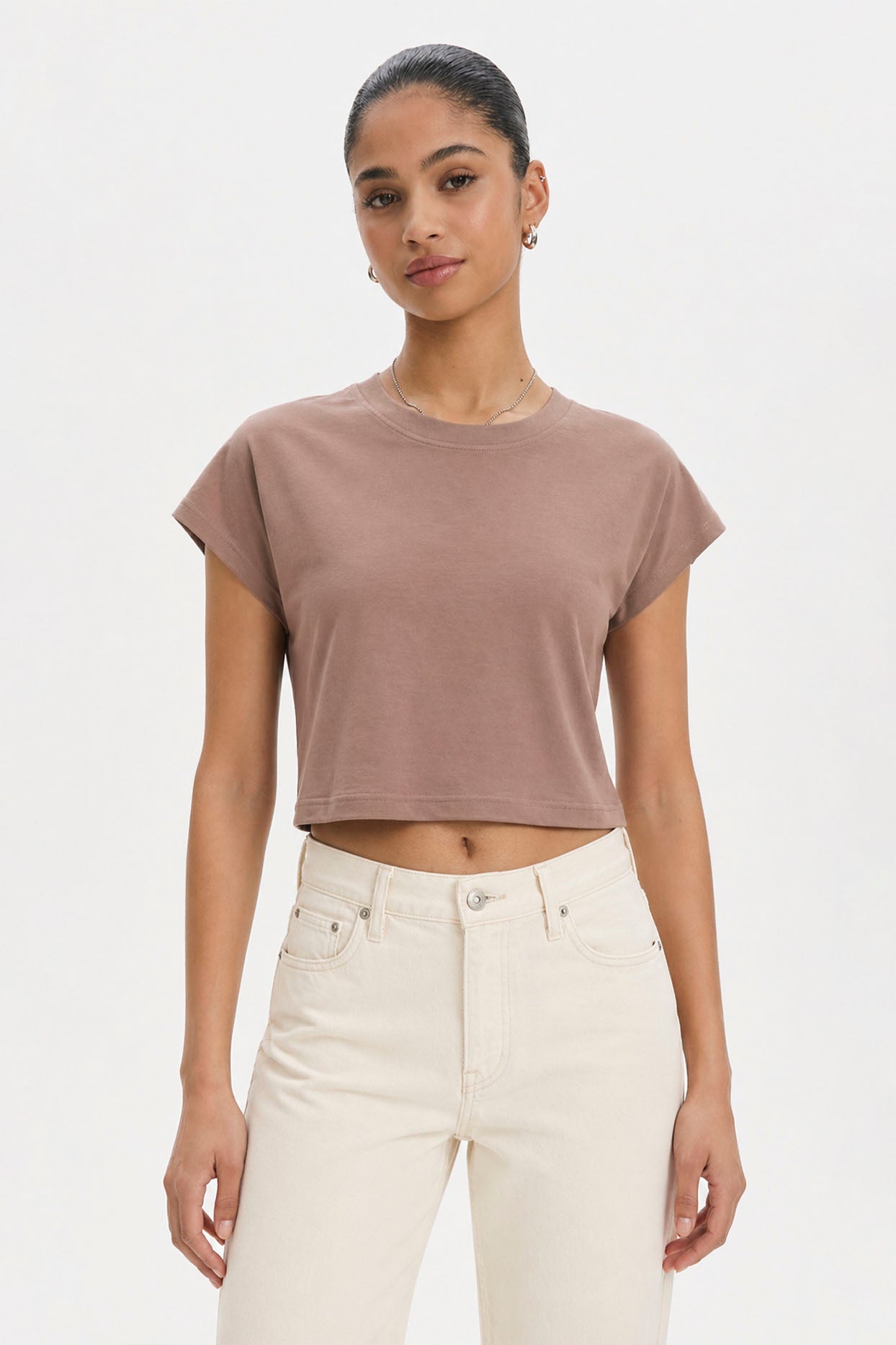Woman wearing a brown cropped t-shirt and white pants on a plain background. brown cotton crop top. aesthetic fashion top. Comfortable cotton crop top in latte brown shade.Basic brown crop top for casual and layered outfits. Trendy brown cotton crop top for women’s fashion store. Soft stretch cotton brown crop top for daily wear. Brown fitted crop top with clean minimal design. Cotton cap sleeve crop top in earthy brown tone.
Women’s latte brown cropped cotton t-shirt top. Casual chic brown cotton crop top