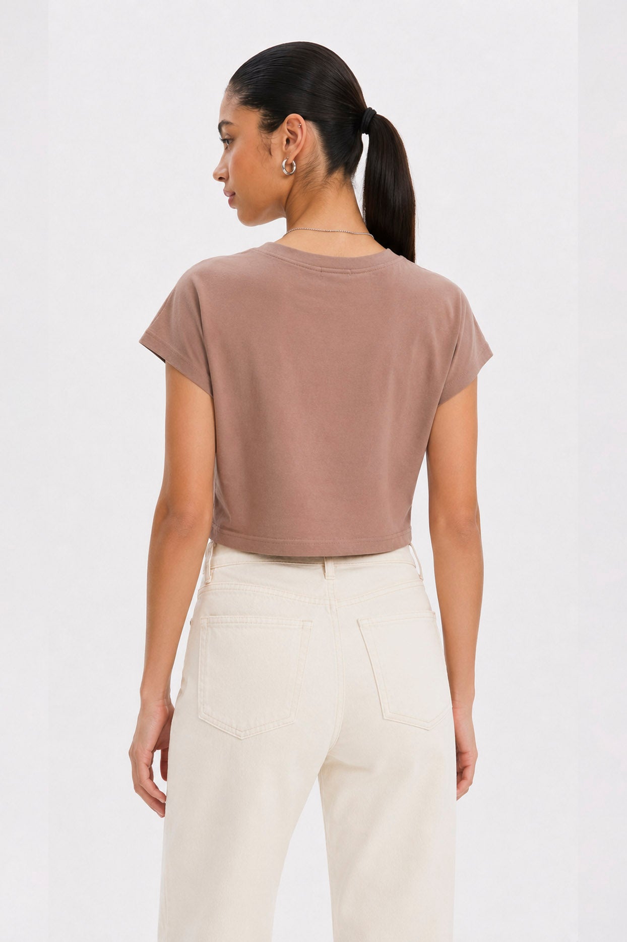 Woman wearing a brown t-shirt and white pants on a white background. brown cotton crop top. aesthetic fashion top. Comfortable cotton crop top in latte brown shade.Basic brown crop top for casual and layered outfits. Trendy brown cotton crop top for women’s fashion store. Soft stretch cotton brown crop top for daily wear. Brown fitted crop top with clean minimal design. Cotton cap sleeve crop top in earthy brown tone.
Women’s latte brown cropped cotton t-shirt top. Casual chic brown cotton crop top for Gen