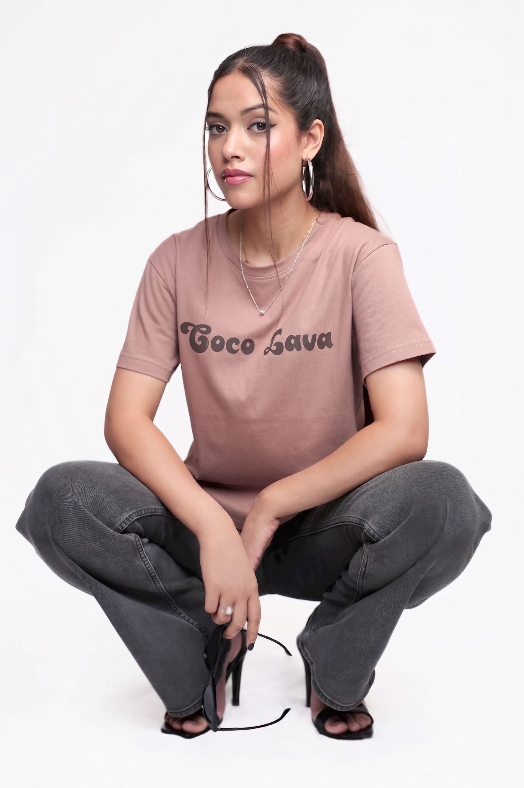 Woman wearing a brown cotton t-shirt with 'Coco Lava' text and black pants sitting on a white background.
GraphicTee, Cotton t-shirt, best cotton t-shirts for summer, brown t-shirt, printed t-shirt, affordable graphic t-shirts women, cute printed cotton tee for daily wear, trendy graphic crop top India, brown graphic cotton t-shirt.