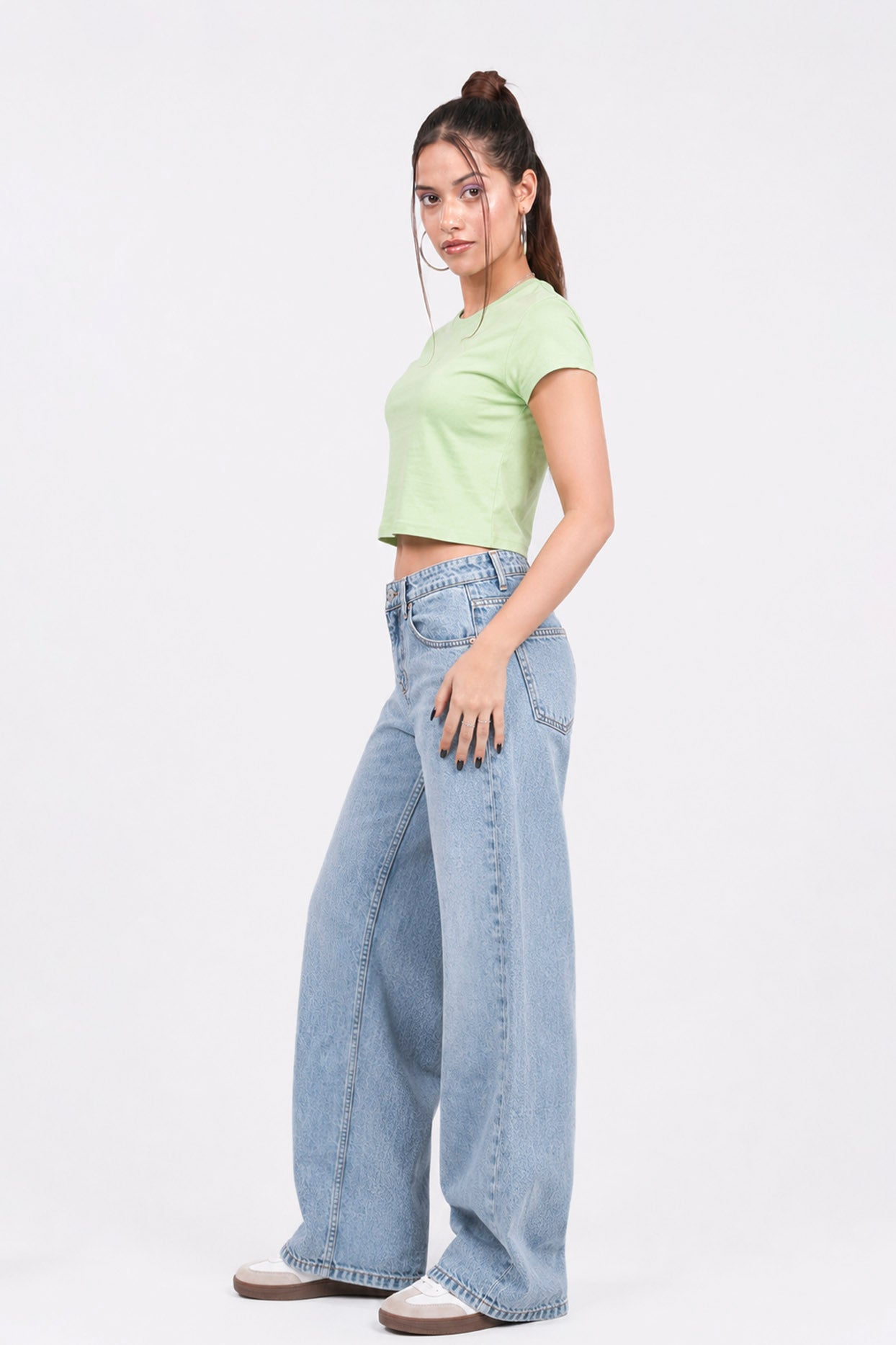 Woman wearing a light green crop top and blue jeans on a white background