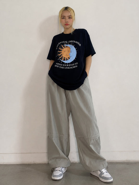 Person wearing a black graphic t-shirt and light gray pants against a plain background
