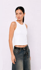 Woman wearing a white sleeveless top and dark jeans on a plain background.white tank top, white tank top women, women's white tank top, sleeveless white top, basic white tank top, white camisole top, white summer top, women's casual top, white fashion top, dark blue denim culottes, denim culottes women, denim jorts women, women's jorts outfit, wide leg denim shorts, knee length denim shorts, blue denim jorts, denim bermuda shorts women, culotte jeans.