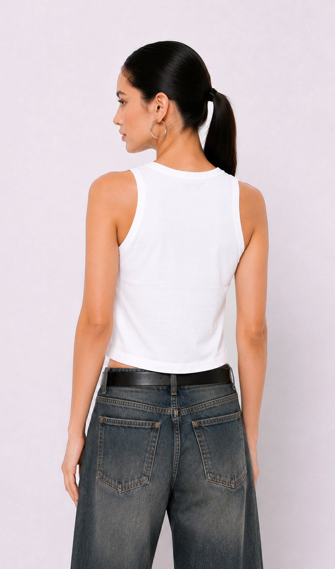 Woman wearing a white sleeveless top and blue jeans against a plain background.white tank top, white tank top women, women's white tank top, sleeveless white top, basic white tank top, white camisole top, white summer top, women's casual top, white fashion top, dark blue denim culottes, denim culottes women, denim jorts women, women's jorts outfit, wide leg denim shorts, knee length denim shorts, blue denim jorts, denim bermuda shorts women, culotte jeans.