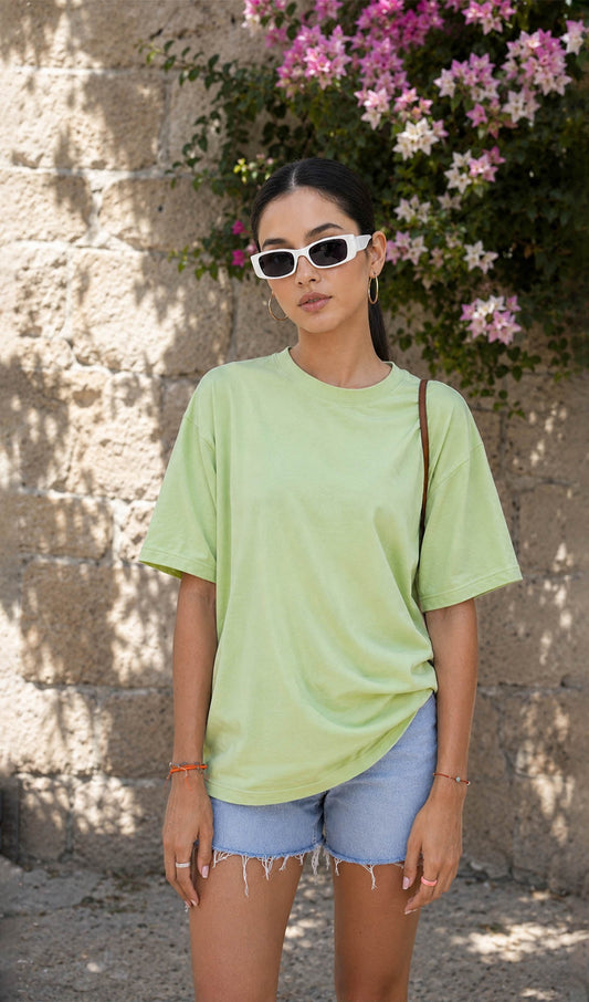 Woman wearing a light green t-shirt and denim shorts standing against a stone wall with flowers.oversized green t-shirt, oversized t-shirt women, oversized cotton t-shirt women,100% cotton oversized t-shirt, Korean fashion t-shirt, gum t-shirt, gym wear, everyday oversized tee