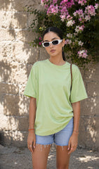 Woman wearing a light green t-shirt and denim shorts standing against a stone wall with flowers.oversized green t-shirt, oversized t-shirt women, oversized cotton t-shirt women,100% cotton oversized t-shirt, Korean fashion t-shirt, gum t-shirt, gym wear, everyday oversized tee