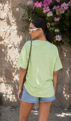 Woman wearing a light green t-shirt and denim shorts standing against a stone wall with flowers.oversized green t-shirt, oversized t-shirt women, oversized cotton t-shirt women,100% cotton oversized t-shirt, Korean fashion t-shirt, gum t-shirt, gym wear, everyday oversized tee