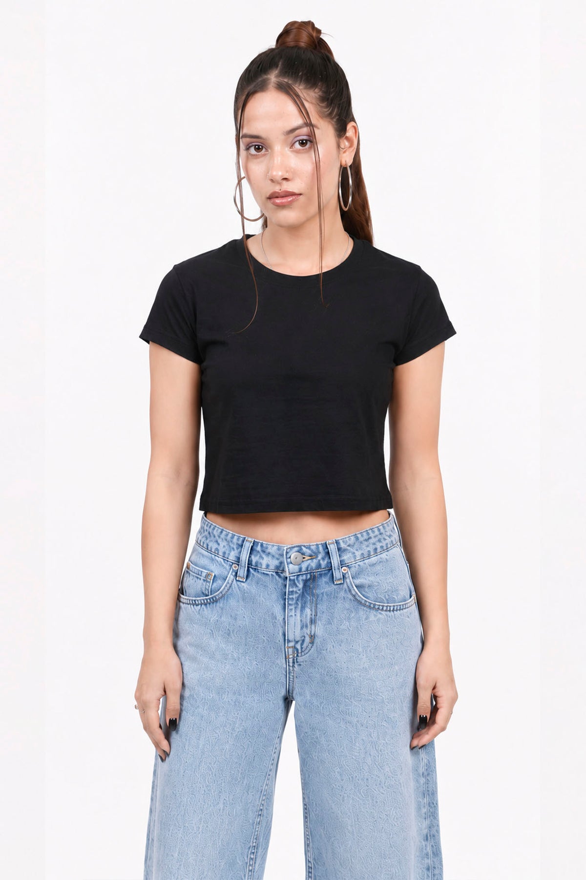 Woman wearing a black crop top and light blue jeans on a white background.black crop top, black crop top women, women's black crop top, black top for women, trendy black crop top, stylish black crop top, casual black crop top, fitted crop top, cropped top women, sleeveless black top, black fashion top, women's fashion top, ladies black top, black crop tank top, summer crop top, trendy women's clothing, casual women's wear, street style outfit, black crop top outfit, blue jeans outfit.