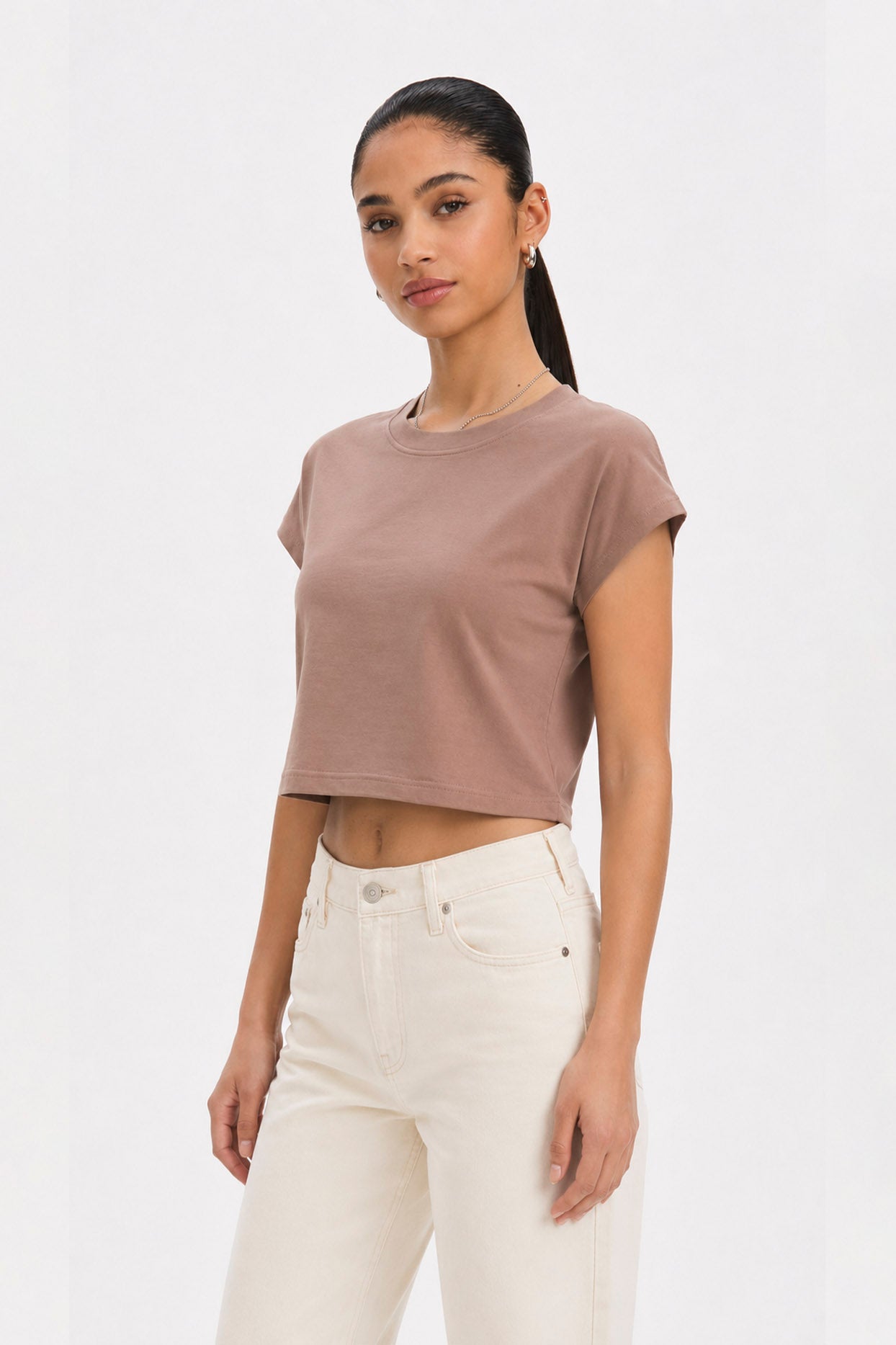 Woman wearing a brown cropped t-shirt and white pants on a plain background. brown cotton crop top. aesthetic fashion top. Comfortable cotton crop top in latte brown shade.Basic brown crop top for casual and layered outfits. Trendy brown cotton crop top for women’s fashion store. Soft stretch cotton brown crop top for daily wear. Brown fitted crop top with clean minimal design. Cotton cap sleeve crop top in earthy brown tone.
Women’s latte brown cropped cotton t-shirt top. Casual chic brown cotton crop top 