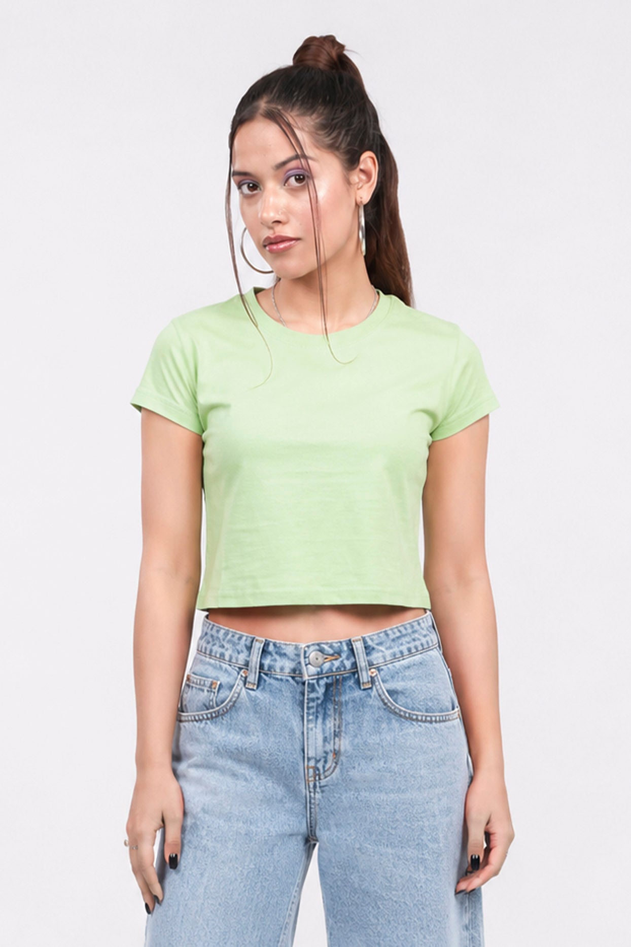 Woman wearing a light green crop top and blue jeans on a white background