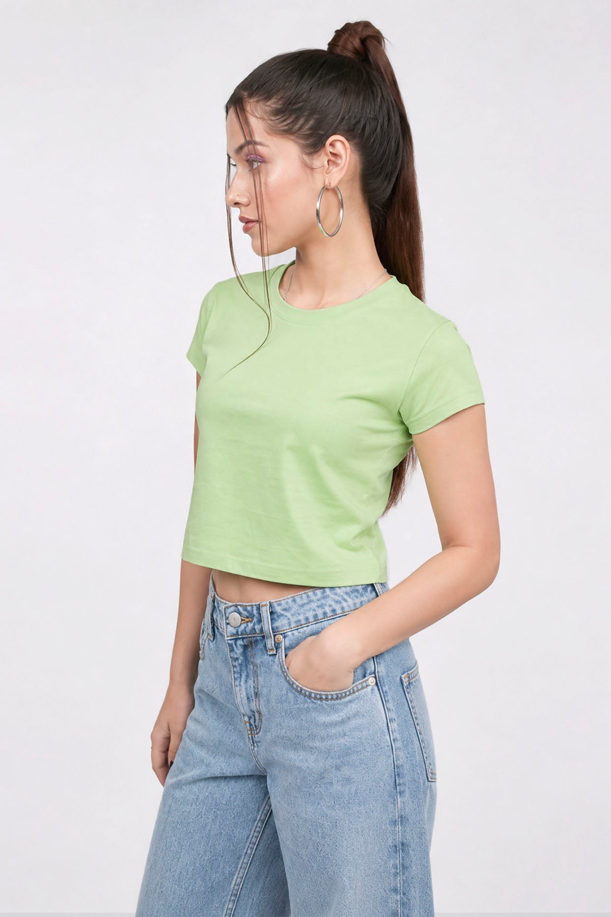 Woman wearing a light green crop top and blue jeans on a white background