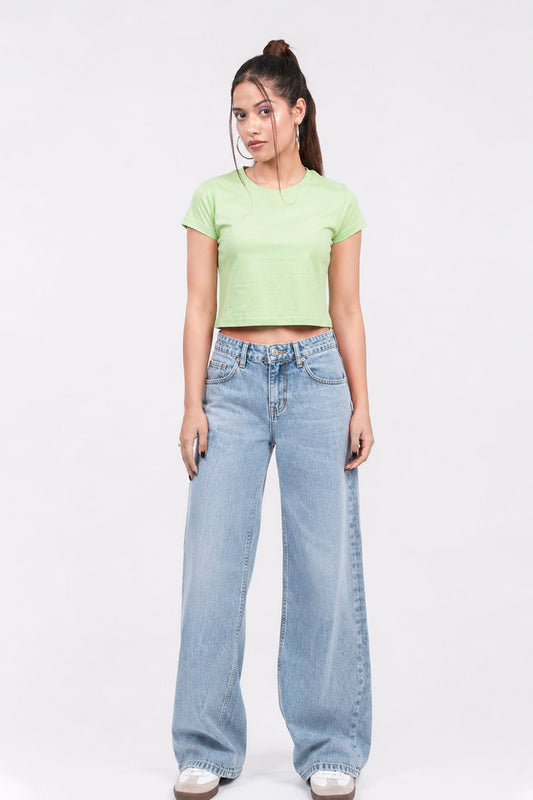 Woman wearing a light green crop top and blue jeans on a white background