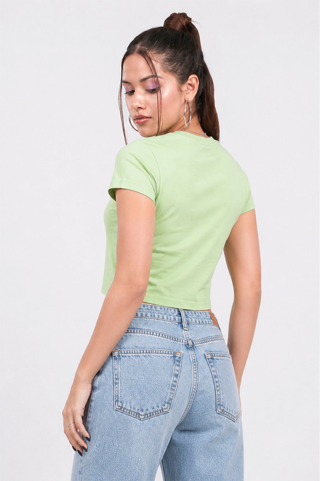 Woman wearing a light green t-shirt and blue jeans on a white background