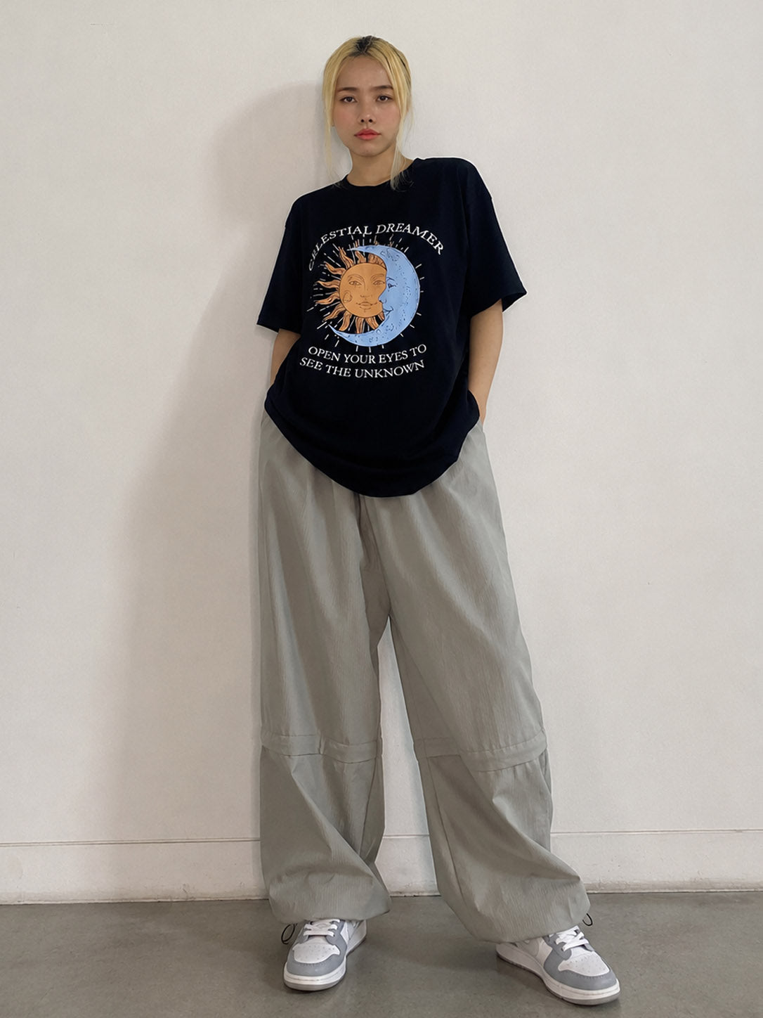 Person wearing a black graphic t-shirt and light gray pants against a plain background