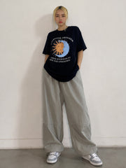 Person wearing a black graphic t-shirt and light gray pants against a plain background