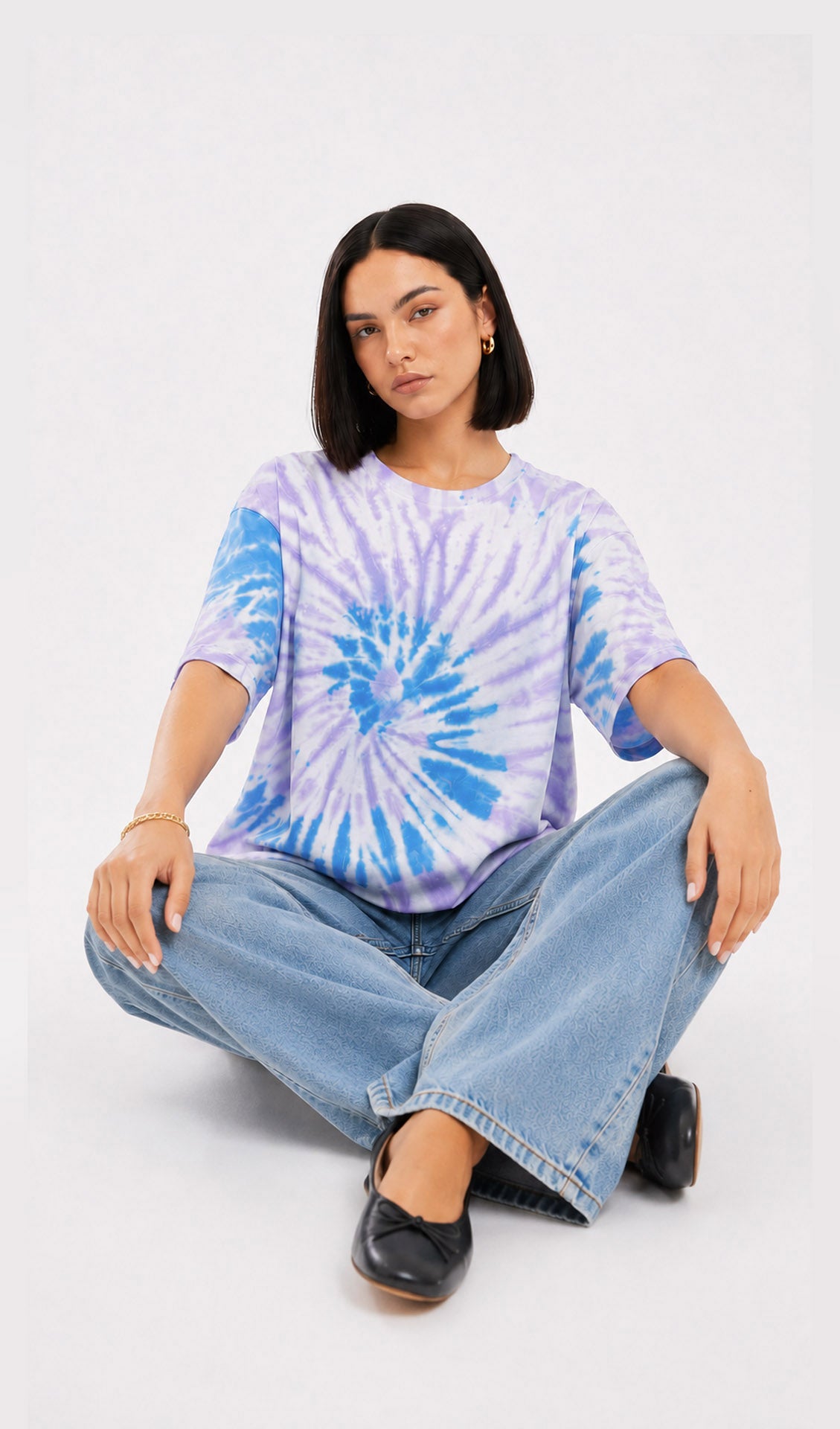 Person wearing a tie-dye shirt and jeans sitting on the floor against a white background.Slayink women Tie & dye tshirt, Slayink women t-Shirt,Oversized T-shirt, Oversized tie & dye T-shirt, oversized t-shirt, trendy college wear,casual wear, pastel top, women workout t-shirt,gym t-shirt women, ladies top, cotton t-shirt, trending top, baggy top, gym tee, loose tshirts for ladies, gym shirt , purple top, tie dye t-shirt women, Soft Girl Fashion, affordable  t-shirt, printed t-shirt women, college wear.