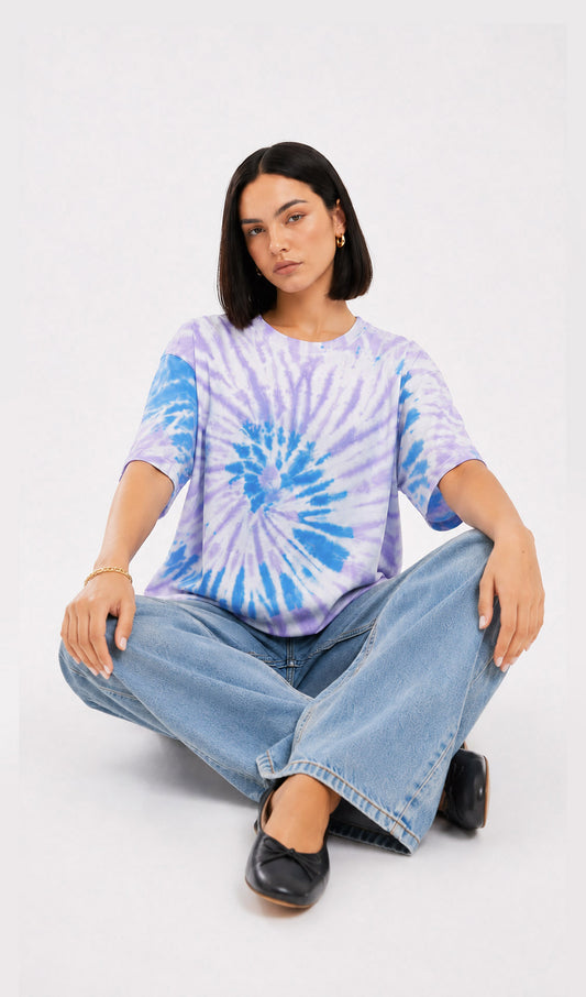 Person wearing a tie-dye shirt and jeans sitting on the floor against a white background.Slayink women Tie & dye tshirt, Slayink women t-Shirt,Oversized T-shirt, Oversized tie & dye T-shirt, oversized t-shirt, trendy college wear,casual wear, pastel top, women workout t-shirt,gym t-shirt women, ladies top, cotton t-shirt, trending top, baggy top, gym tee, loose tshirts for ladies, gym shirt , purple top, tie dye t-shirt women, Soft Girl Fashion, affordable  t-shirt, printed t-shirt women, college wear.
