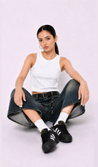 Woman wearing a white tank top, blue jeans, and black Adidas shoes on a white background.white tank top, white tank top women, women's white tank top, sleeveless white top, basic white tank top, white camisole top, white summer top, women's casual top, white fashion top, dark blue denim culottes, denim culottes women, denim jorts women, women's jorts outfit, wide leg denim shorts, knee length denim shorts, blue denim jorts, denim bermuda shorts women, culotte jeans.